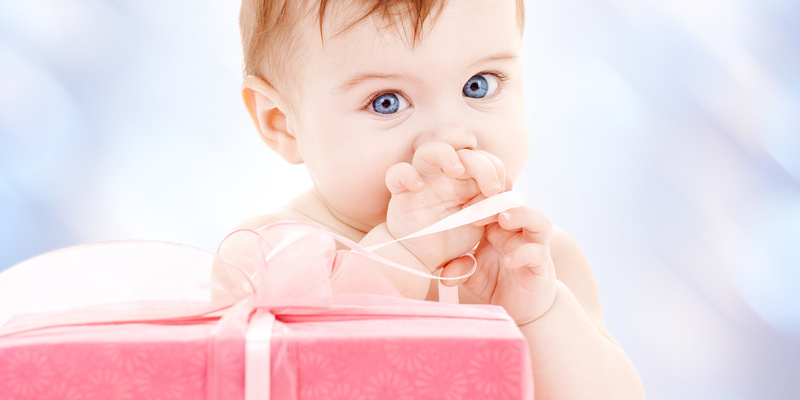 Baby mit Geschenk / © stock.adobe.com/Syda Productions Baby staunt über ein noch verpacktes Geschenk